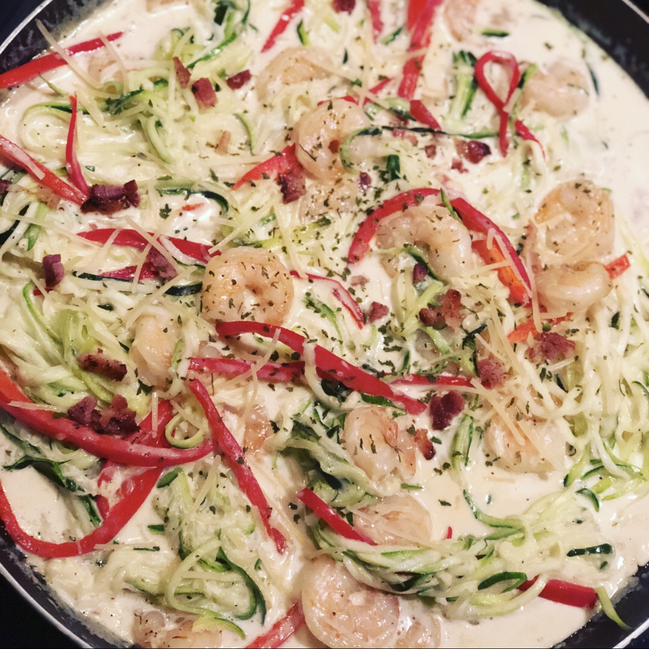 Spiral zucchini noodles in a white sauce with shrimp and sliced red bell peppers