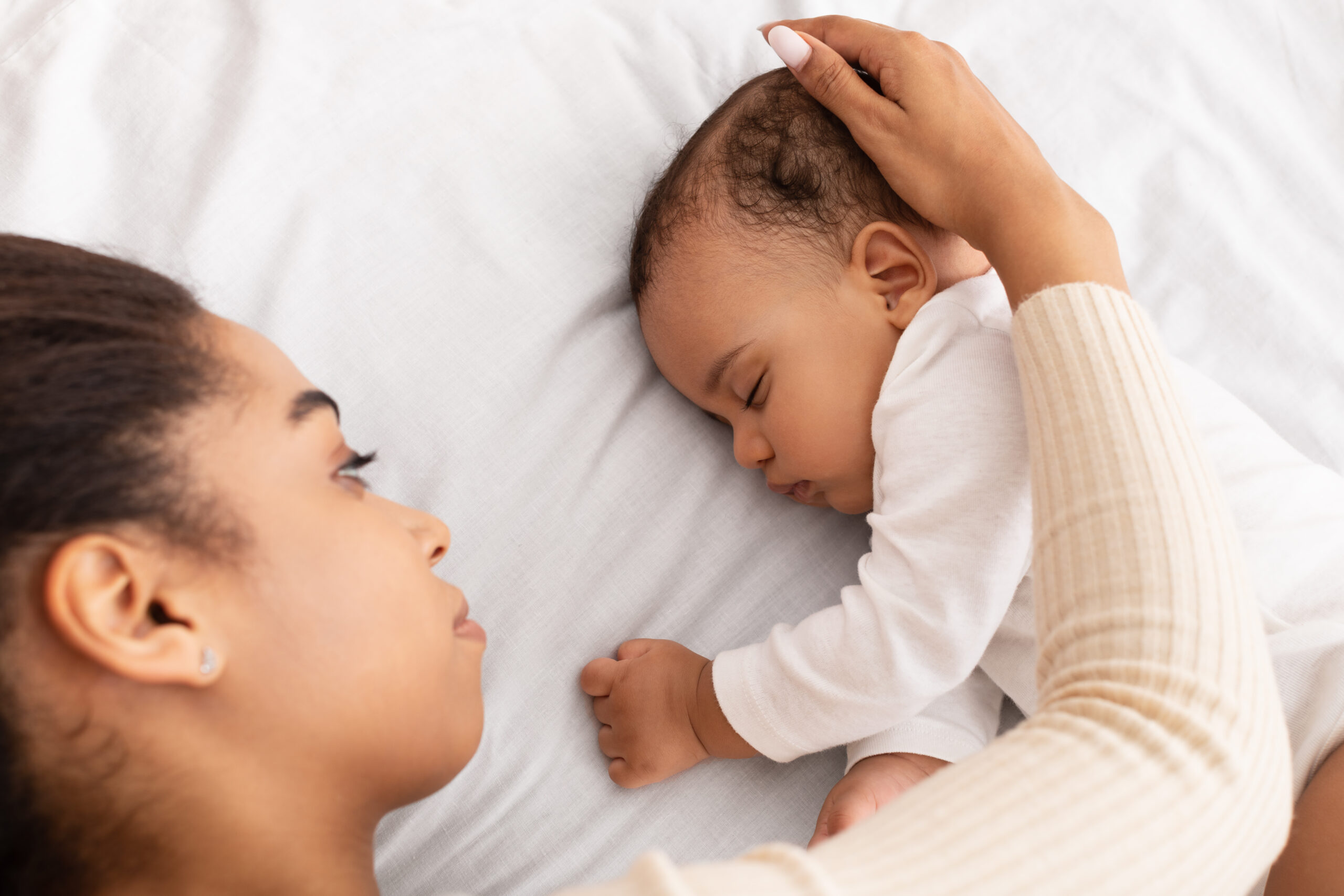 Black mom stroking sleeping baby head as they lay down together