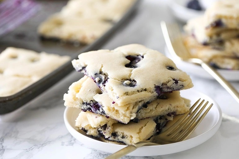 Squares of blueberry pancakes stacked on a white plate