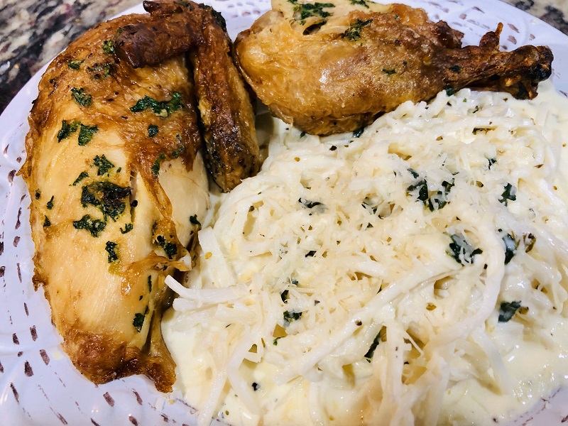 A heap of hot alfredo hearts of palm pasta noodles on white plate with two pieces of chicken