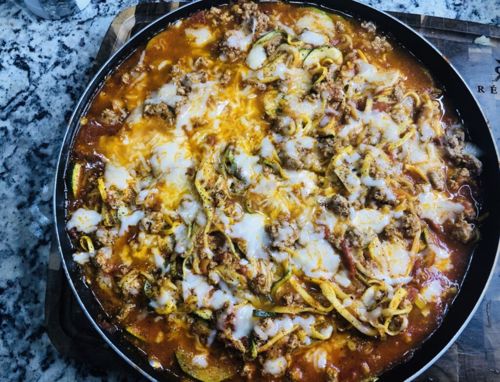 Zucchini noodles in a skillet with ground meat, red sauce and melted cheese