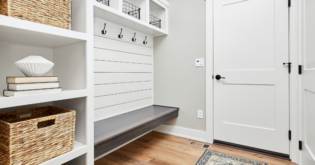 Organized mudroom, white and light gray walls, wood floors with wicker basket accents.