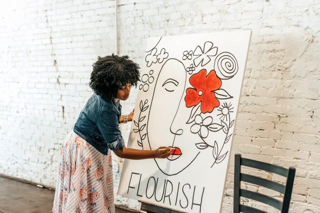 A woman with a curly fro painting a large piece of artwork with the words "flourish"